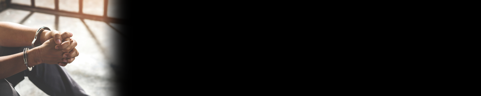 Imagem de uma pessoa sentada dentro da prisão, algemada.